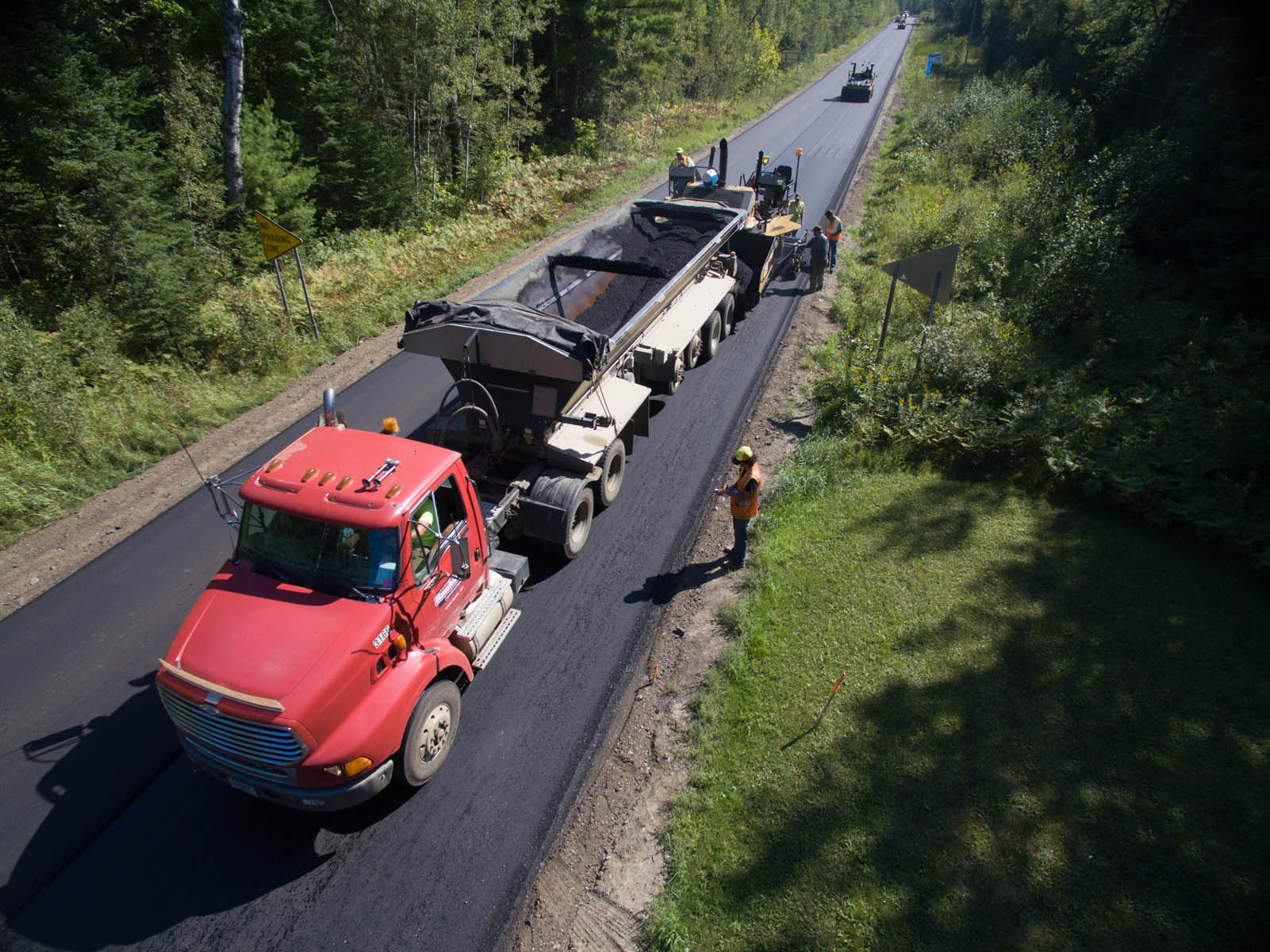 Birds-eye view of dump truck hauling and dumping asphalt on country road
