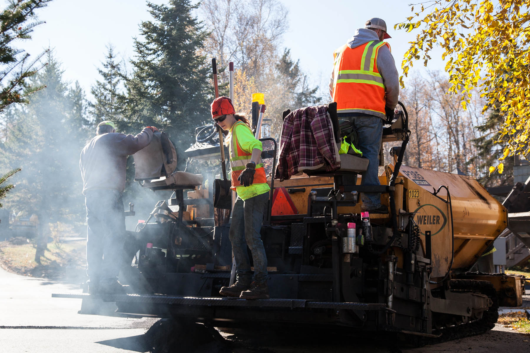 Employees riding heavy machinery handling asphalt