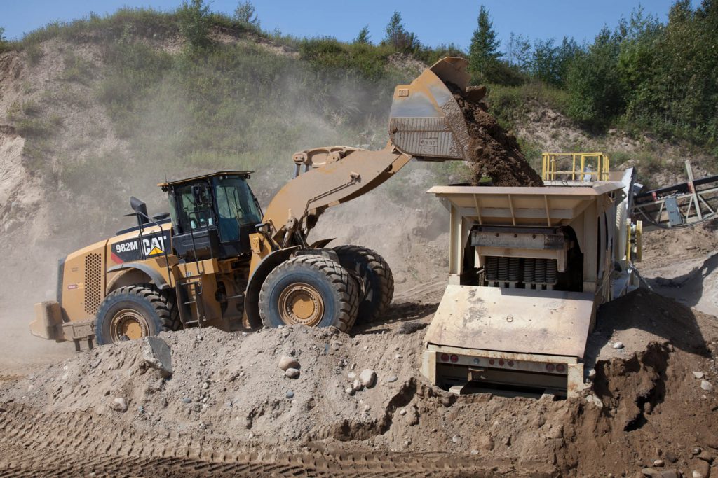Front-end loader pouring aggregate into a giant funnel on another machine