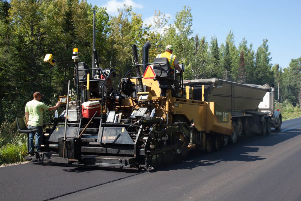 Employees riding heavy machinery laying asphalt