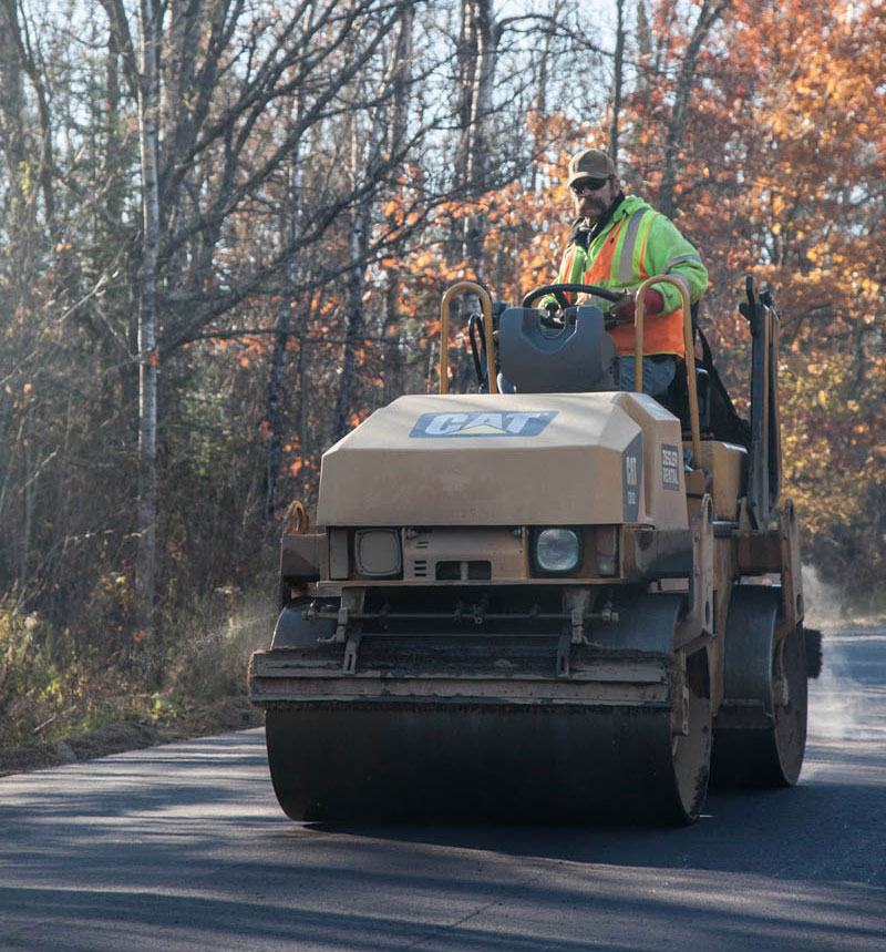 Employee driving Caterpillar steamroller flattening fresh asphalt on country road